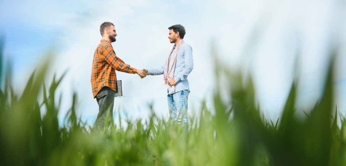 The concept of international relations in agrarian business. Indian and European farmers stand in a field of green wheat.
